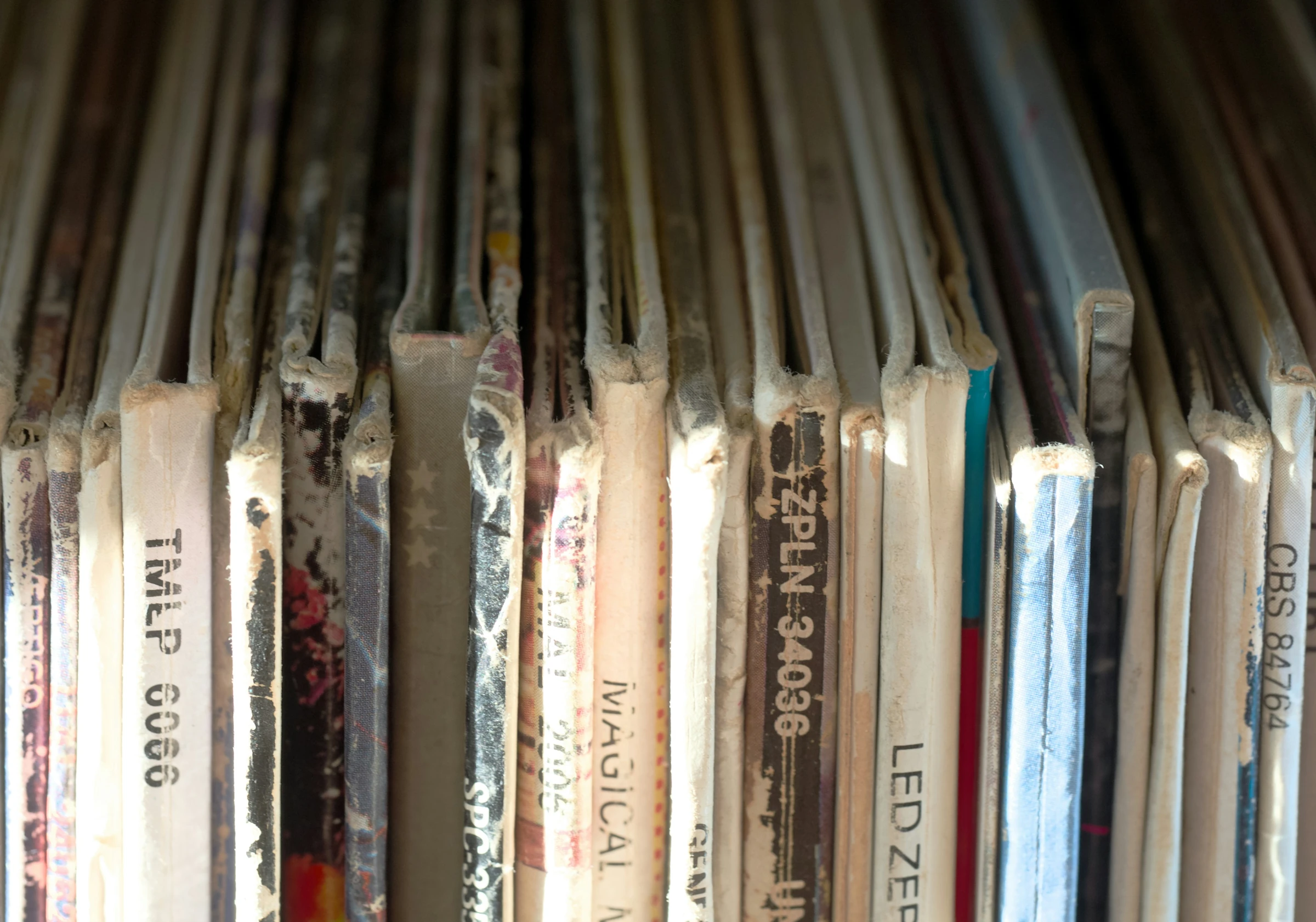 Gros plan sur les tranches usées de pochettes de vinyles, éclairées par le soleil.
